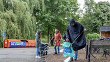 In de regen zijn drie deelnemers in regenpak bezig met zwerfafval rapen.