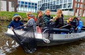 Jongeren op een klein bootje met schepnetten die plastic uit het water vissen