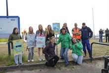 Een groep scholieren poseert samen met Mieke van der Wal met zelfgemaakt borden tegen zwerfafval.