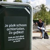 Afvalbak met campagnetekst 'Je plek schoon achterlaten. Zo gefikst. Ook als het afval van je vrienden is. Ja toch!'